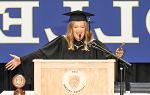 Student Rosie Luke wearing graduation regalia while standing at podium spreading her arms wide in celebration