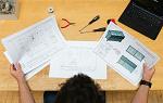 A person sitting at a desk reviewing three technical papers.