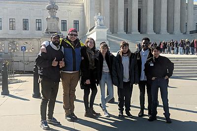 A group of 7 students of various genders and ethnicities pose for a picture outside the African-American Museum of History and Culture in Washington DC. 